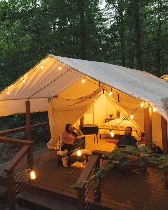 two campers sitting on the porch of glamping yurt tent with string lights at rustic acres