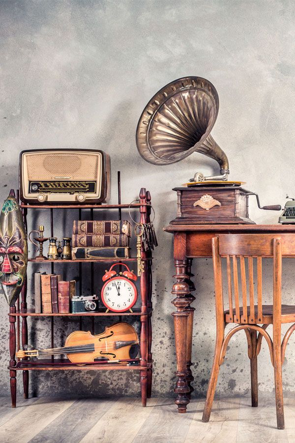 Antique chair, old typewriter, retro radio, gramophone on wooden desk, books, clock, camera, binoculars, fiddle, keys on shelf, mask, cylinder hat, shoes, cane, backpack. Vintage style filtered photo